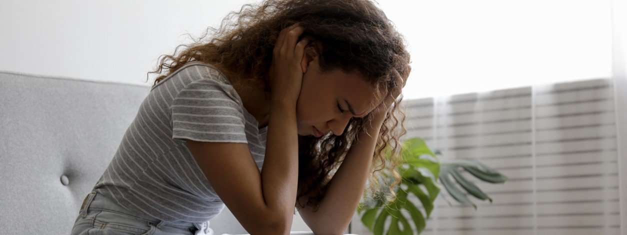 An Schizophrenie leidende junge Frau sitzt auf dem Sofa und hält sich den Kopf.