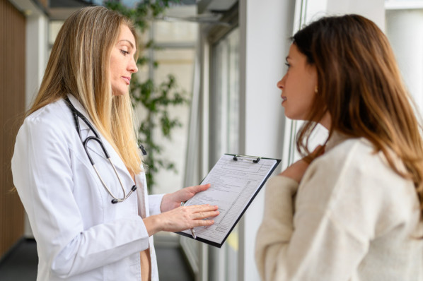 Female doctor in lab coat showing and discussing medical test results with patient in hospital during consultation