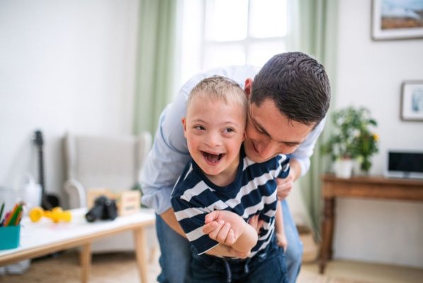Ein Vater umarmt seinen etwa 7 jährigen Sohn mit Down-Syndrom.