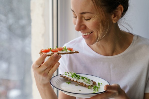 Eine etwa 30 jährige Frau genießt Microgreens auf einem Knäckebrot mit Quark oder Frischkäse