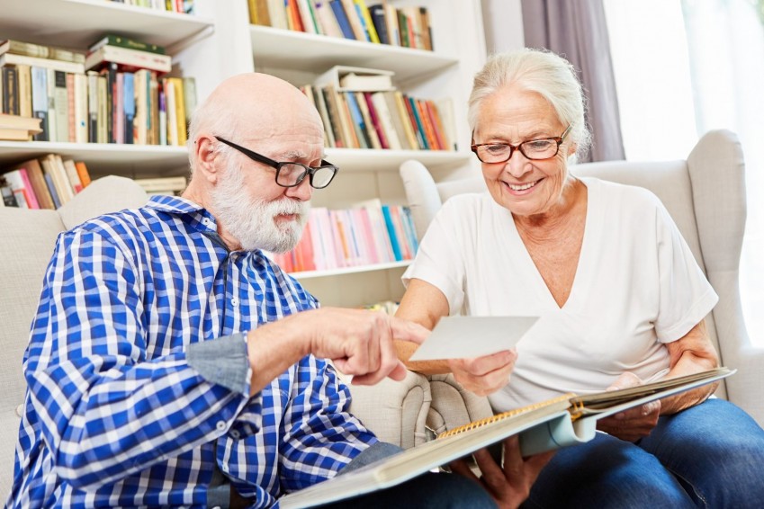 Ein Seniorenpaar sitzt auf einer Couch und schaut sich gemeinsam ein Fotoalbum an. Beide lächeln.