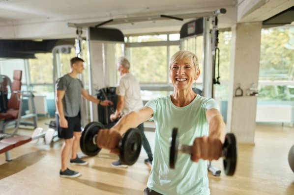 Eine ältere Frau trainiert mit Gewichten im Fitnessstudio.
