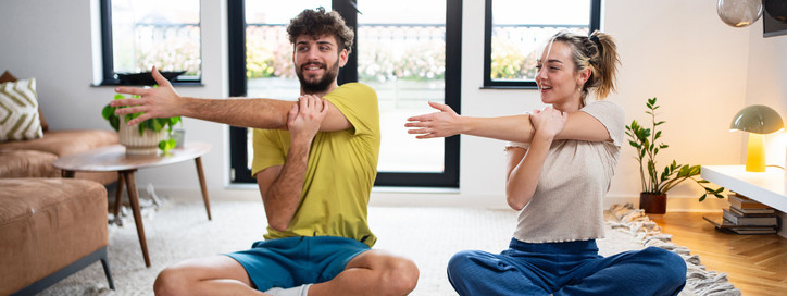 Ein Paar macht Zuhause Mobilitätsübungen für die Arme im Schneidersitz.