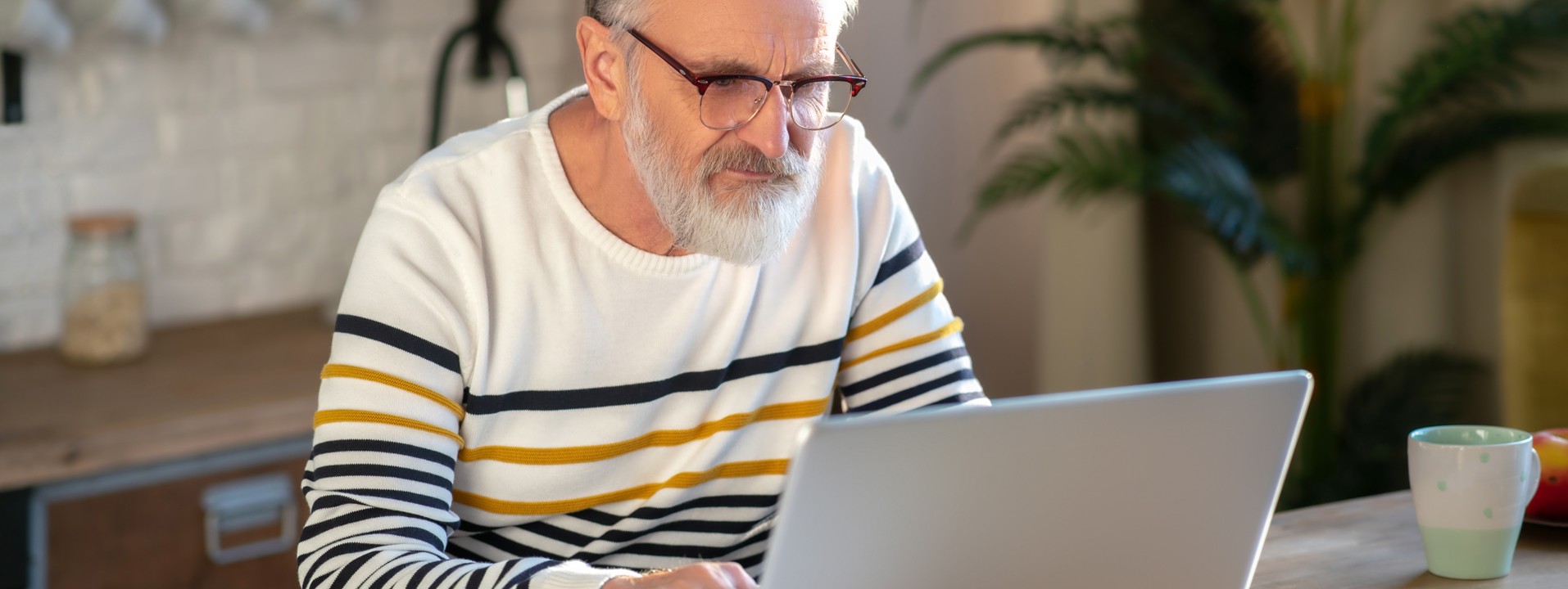 Ein etwa 60-jähriger Mann sitzt zu Hause am Tisch vor dem Laptop.