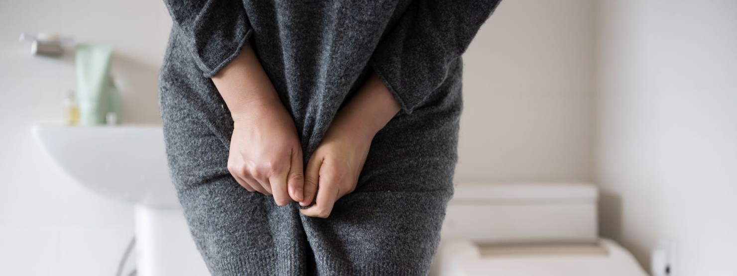 Eine junge Frau steht vor der Toilette. Ihr schmerzt der Unterleib. 