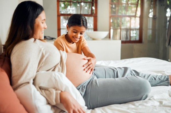 Eine Tochter streichelt begeistert den schwangeren Bauch ihrer Mutter