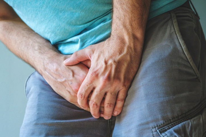 Ein Mann leidet unter Mycoplasma genitalium und hält sich den Schritt