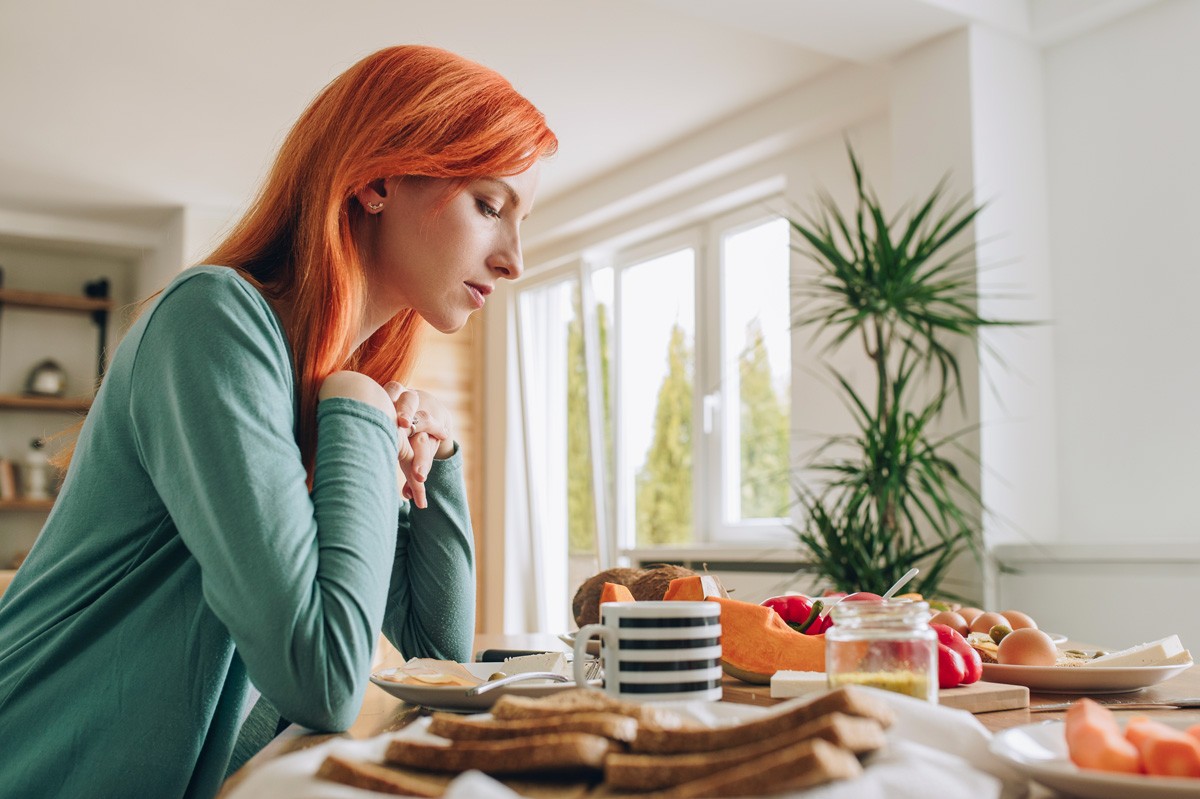 Etwa 25-jährige Frau schaut nachdenklich auf den gedeckten Frühstückstisch.