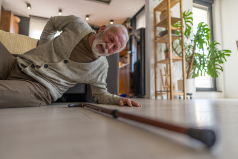 Senior, der unter Schmerzen leidet und Schwierigkeiten hat, aufzustehen, nachdem er zu Hause hingefallen ist