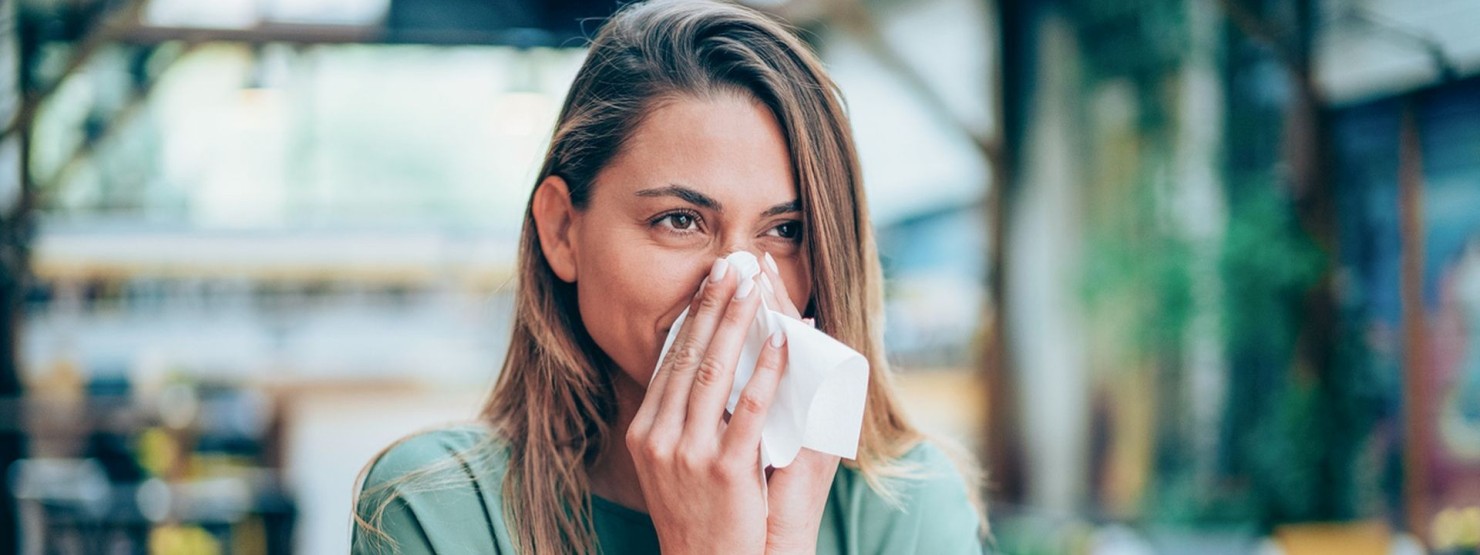 Eine Frau putzt sich aufgrund einer Pollenallergie die Nase.