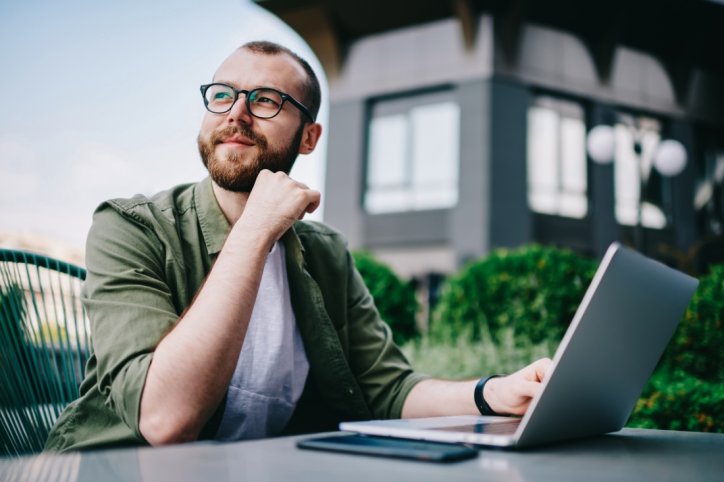 Ein mann Mitte 30 arbeitet am laptop und schaut zuversichtlich zur Seite