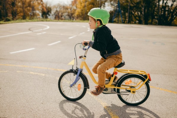 Eine Vater bringt seiner etwa 6 jährigen Tochter auf einer asphaltierten Allee das Fahrradfahren bei.