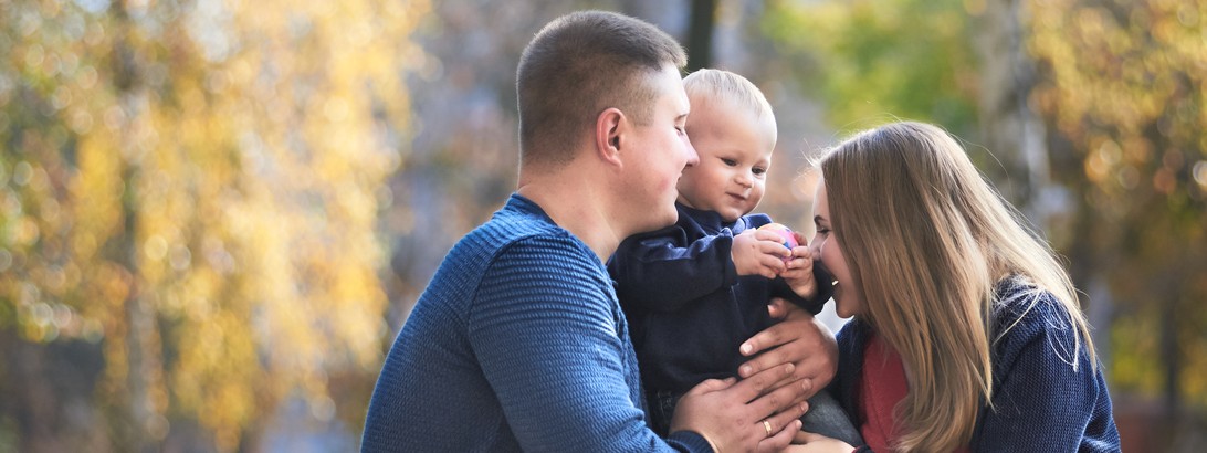 Eine dreiköpfige Familie sitzt auf einer Wiese und spielt und lacht gemeinsam.