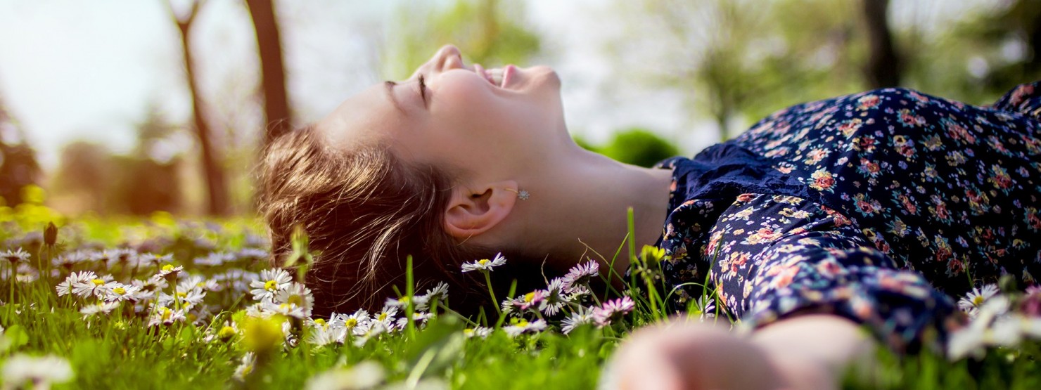 Frau liegt lächelnd auf der Blumenwiese und genießt die Sonne.