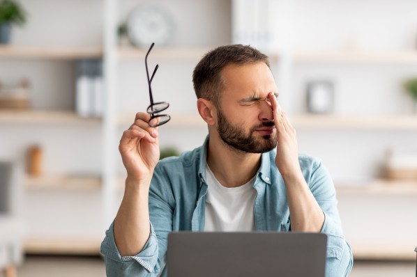 Ein Mann Anfang 30 reibt sich das Auge nach Arbeit am Computerbildschirm