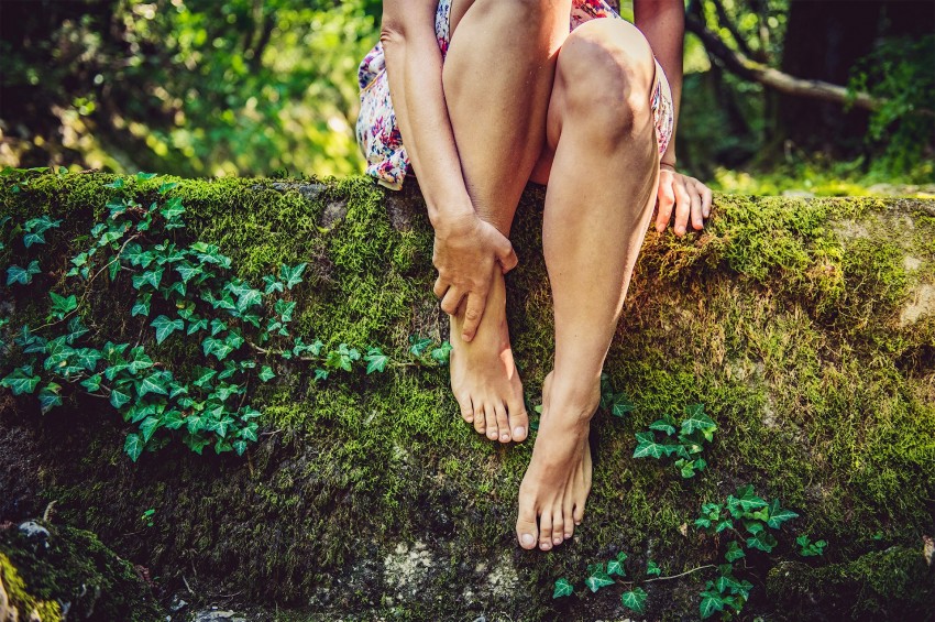 junge Frau berührt ihren nakten Fuß im Wald