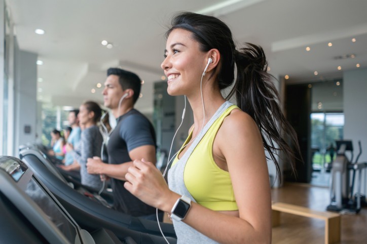 Eine etwa 30-jährige Frau läuft zusammen mit anderen Personen auf einem Laufband im Fitnessstudio.