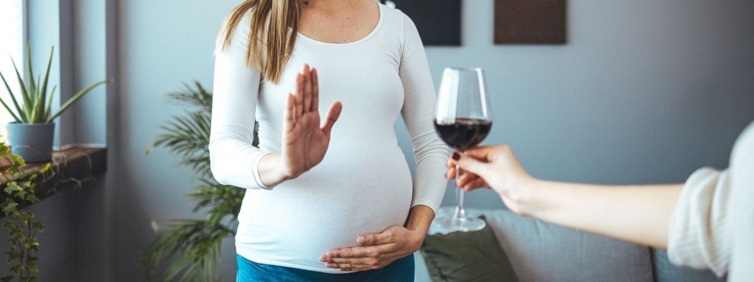 Einer schwangeren Frau wird ein Glas Wein angeboten. Sie lehnt dankend ab.