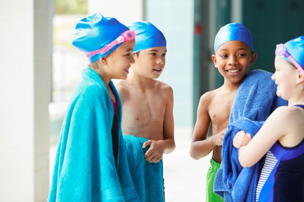 Vier etwa 10-jährige Kinder stehen im Schwimmbad in ihre Badetücher eingewickelt zusammen.