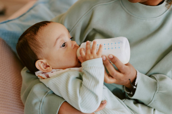 Mutter hält Baby im Arm. Baby trinkt aus Flasche