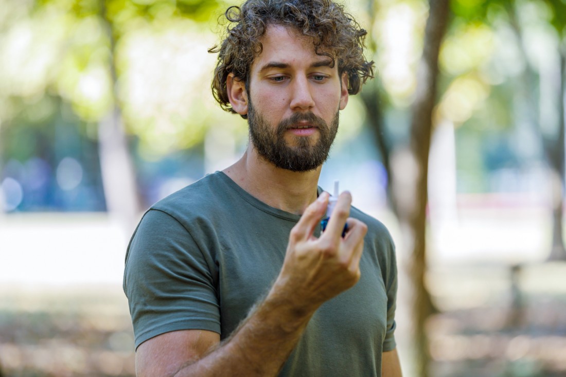A Man with Breathing Problems is Feeling Displeased and Using a Nasal Spray During a Walk in City Park During a Summer Day.
