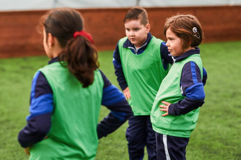 Drei Kinder stehen auf einem Rasen, habe grüne Trikots an und machen Sport.