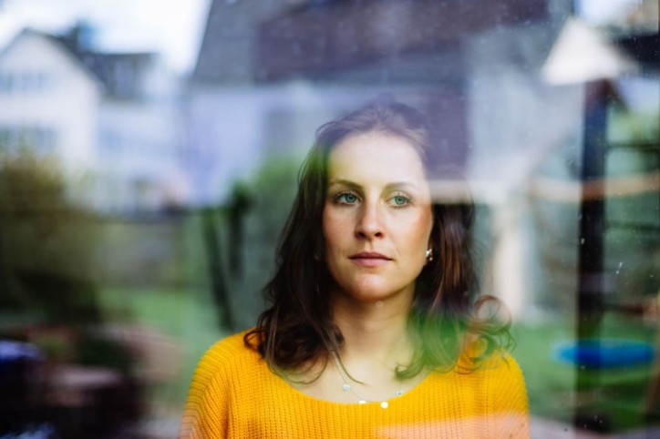 Eine Frau mit Tränensäcken schaut aus dem Fenster