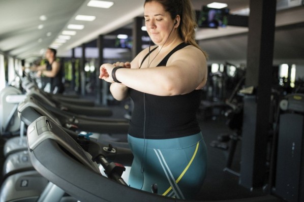 Eine junge Frau steht im Fitnessstudio auf dem Laufband.