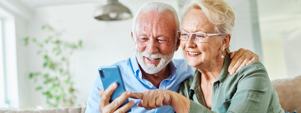 Zwei Senioren schauen auf ihr Handy und melden sich bei der Infoveranstaltung "Gesund im Alter" in Dessau an.