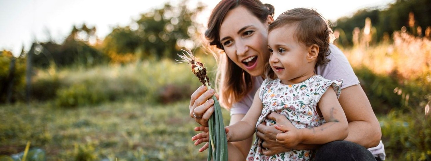 Eine Mutter zeigt ihrer kleinen Tochter eine frisch gepflückte Lauchzwiebel.