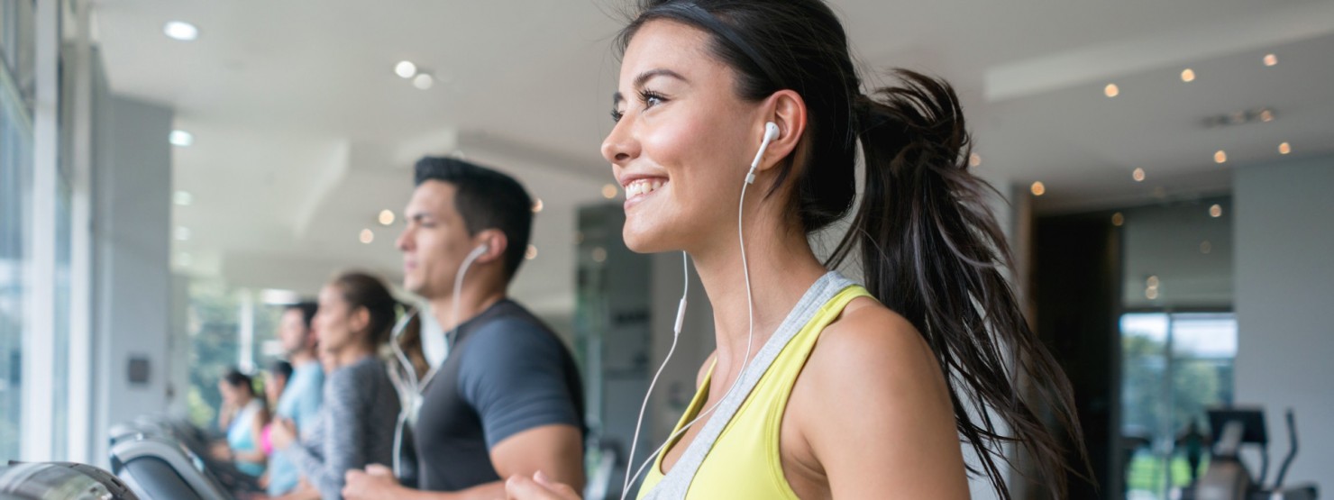 Eine etwa 30-jährige Frau läuft zusammen mit anderen Personen auf einem Laufband im Fitnessstudio.