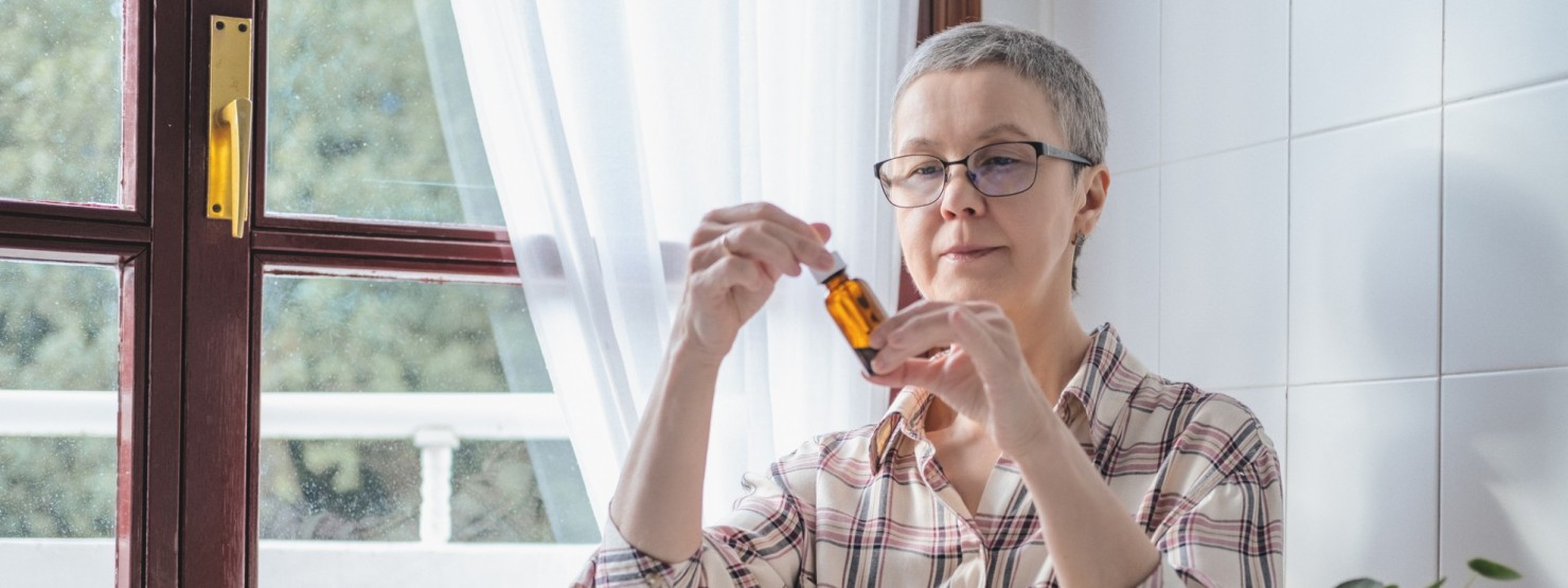 Eine Seniorin in roten Pullover steht in einer Apotheke und lässt sich von einer Apothekerin beraten. Sie lächelt.
