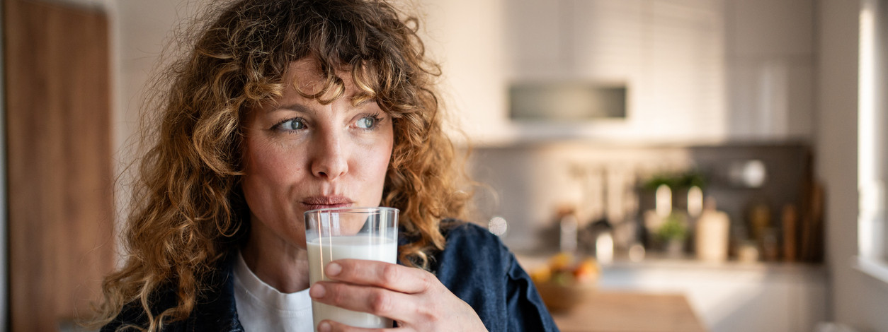 Thoughtful mid-adult woman sipping a glass of milk in her modern kitchen, savoring a refreshing and nutritious start to her day while enjoying the simple pleasures of morning routine