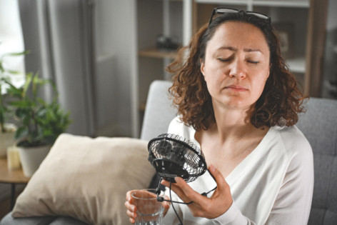 Eine Frau versucht Hitzepickel zu verhindern indem sie sich mit einem Ventilator abkühlt.