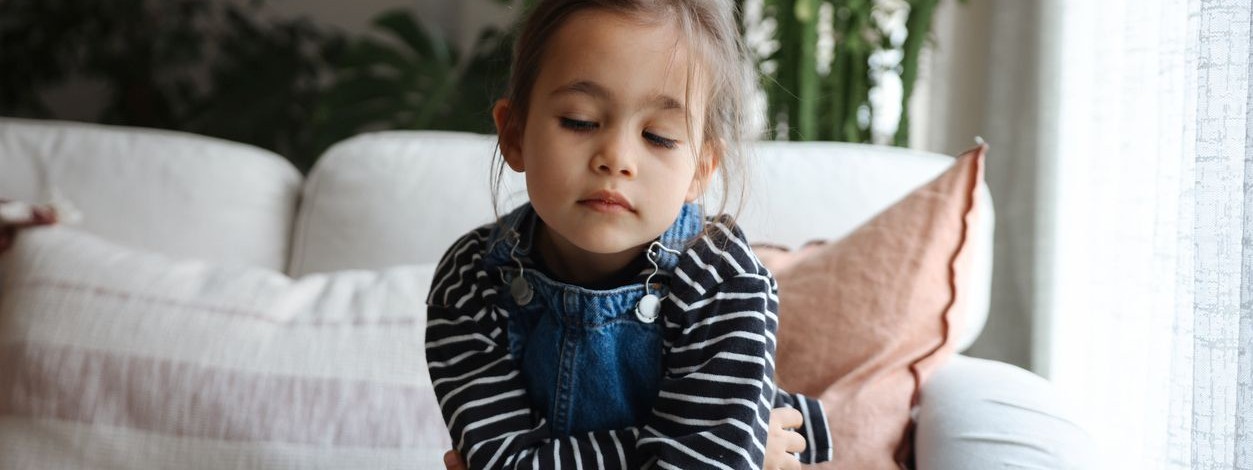 Ein etwa 4-jähriges Mädchen sitzt mit Bauchschmerzen auf der Couch.
