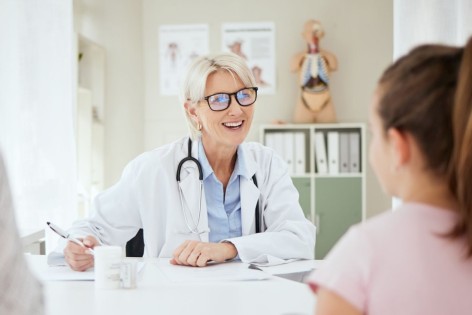 Eine etwa 50 jährige-Ärztin spricht mit einer Patientin und deren Mutter im Behandlungszimmer. Alle drei sitzen am Tisch.