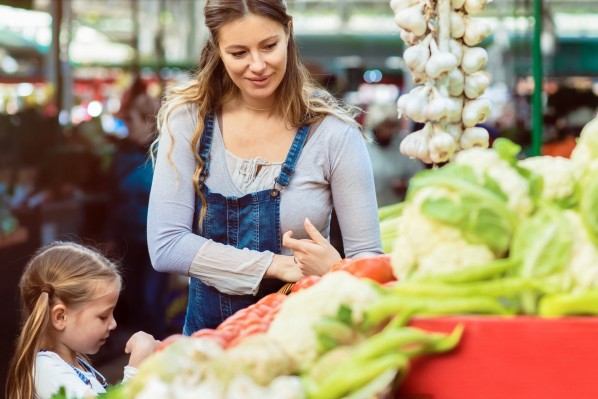 Eine circa 30-jährige, schwangere Frau kauft mit ihrer circa 7-jährigen Tochter frisches Gemüse auf dem Markt.