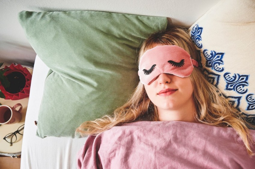 junge Frau Anfang 20 liegt mit einer Schlafmaske im bett