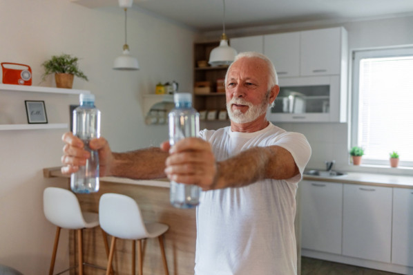 älterer mann macht hantelübung mit 2 wasserflaschen