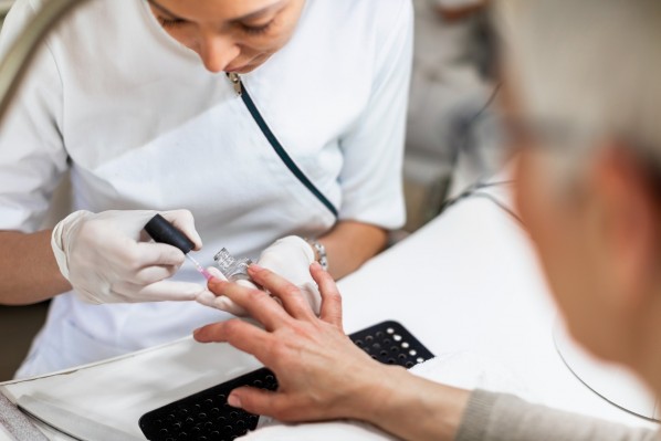 Eine Krankenschwester, 30 Jahre, trägt Antipilz-Nagellack auf die Fingernägel einer Patientin auf.