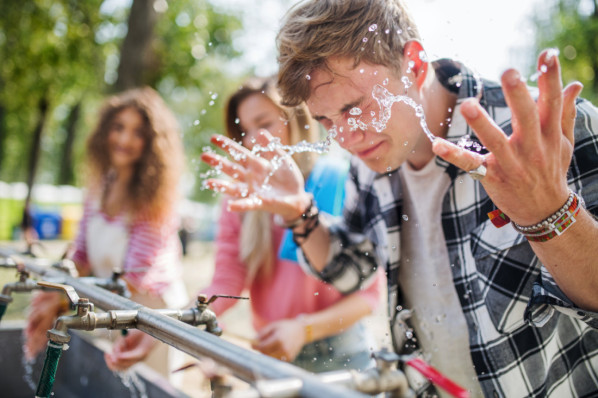 Junger Mann spritzt sich beim Festival an Sanitärstation Wasser ins Gesicht.