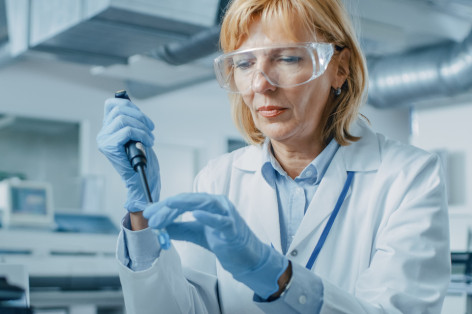 Eine Laborantin füllt mit Hilfe eine Mikropipette eine Flüssigkeit in ein Teströhrchen ab.