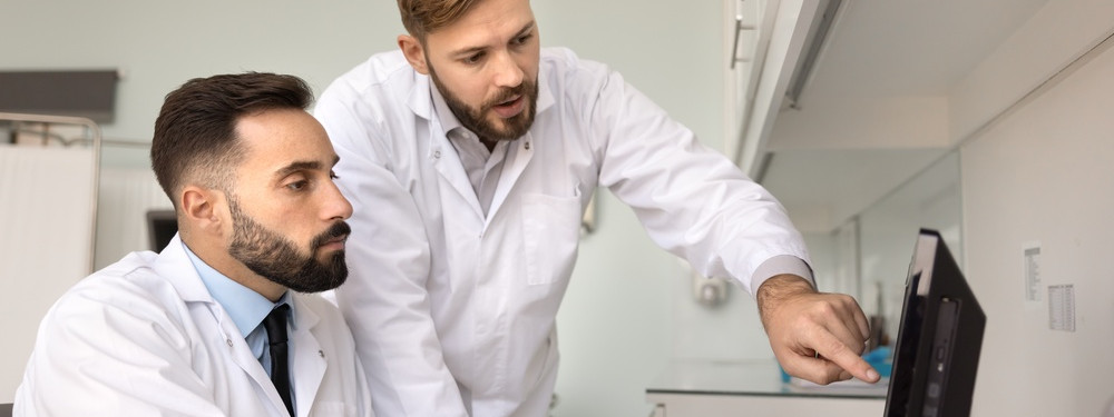 Zwei Ärzte schauen sich gemeinsam auf einem Computer die Befunde eines Patienten an.