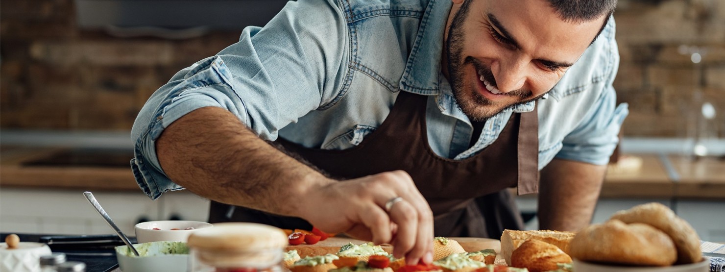 Ein etwa 35-jähriger Mann belegt Baguettescheiben mit Gemüse.