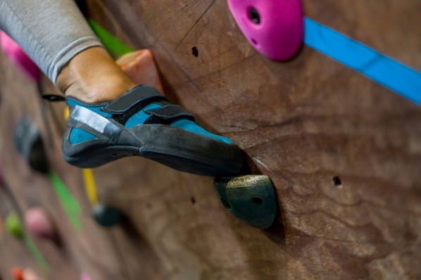 Eine Junge Frau klettert mit speziellen Boulder-Schuhen in einer Boulderhalle.