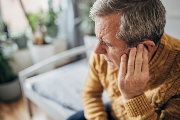 Ein Senior leidet unter Misophonie und fässt sich an sein linkes Ohr.
