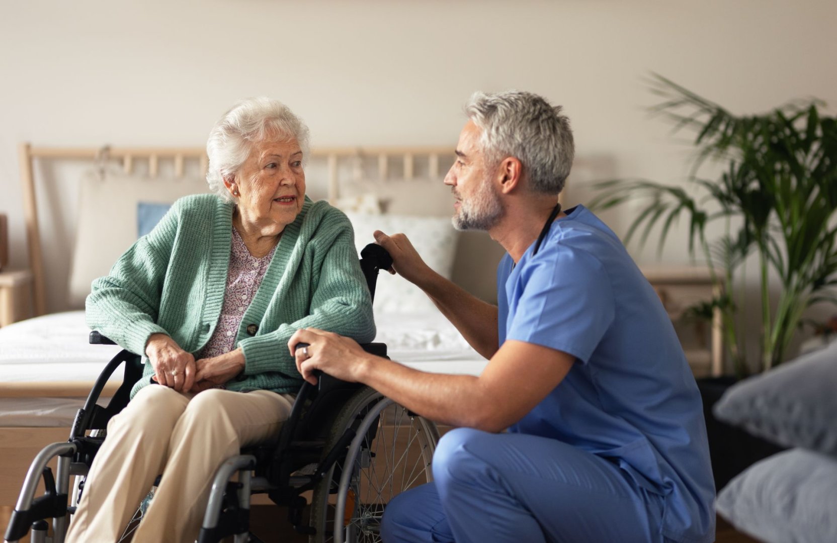 Ein Pfleger spricht mit einer Seniorin im Rollstuhl.