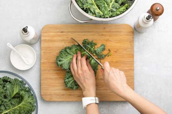 Fresh kale leaves are cut by woman's hands on a cutting board, healthy or clean eating concept, overhead view image