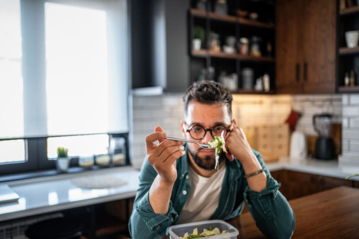 Ein junger Mann betrachtet desinteressiert seinen Salat
