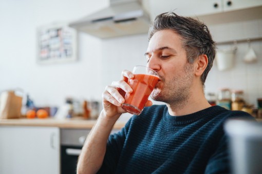 Ein etwa 40-jähriger Mann sitzt in seiner Küche und trinkt ein Glas Fruchtsaft.